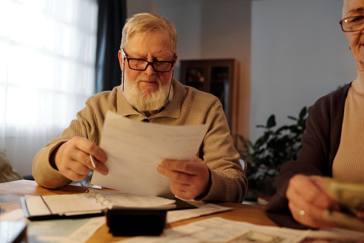 Senior man reading winter fuel payment document at wooden table